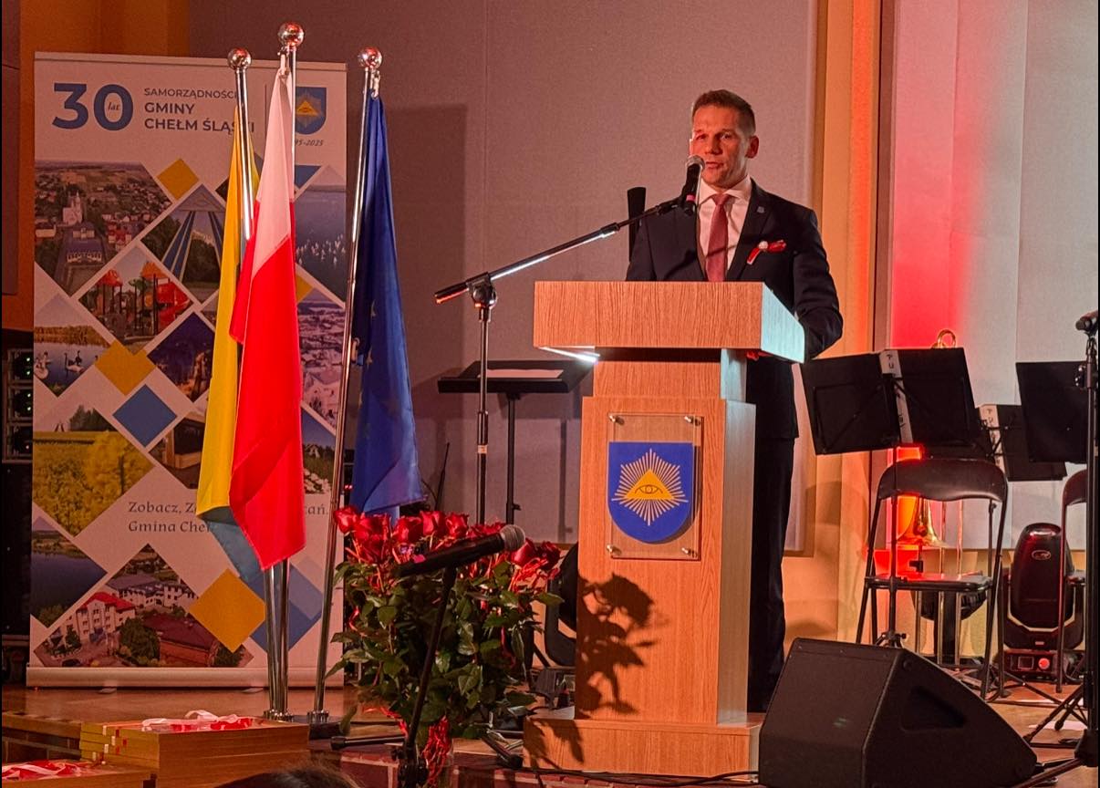 Mężczyzna stojący za mównicą na scenie w sali koncertowej